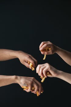 A conceptual image featuring several hands holding french fries against a dark backdrop, emphasizing fast food culture.