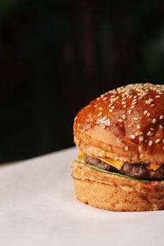 Close-up of a mouth-watering cheeseburger on parchment paper with sesame seed bun.