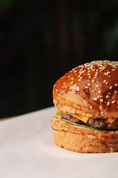 Free Close-up of a mouth-watering cheeseburger on parchment paper with sesame seed bun. Stock Photo