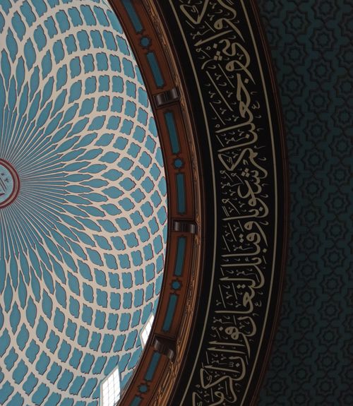 Free Detailed view of Islamic calligraphy decorating a blue dome ceiling with geometric patterns. Stock Photo