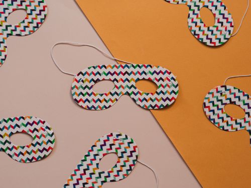 Free Colorful paper masks with zigzag patterns on a diagonal yellow surface, perfect for parties. Stock Photo