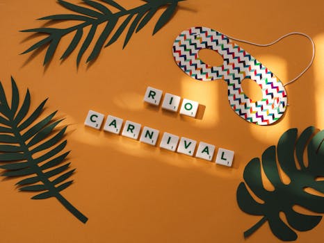 Colorful paper mask and RIO CARNIVAL text on yellow surface with green leaves.
