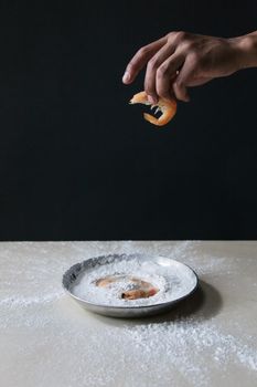 Close-up of a hand holding shrimp above a flour-filled bowl on a table.