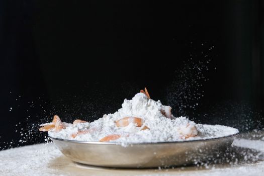 A bowl of shrimps being coated with flour, ready for cooking preparation.