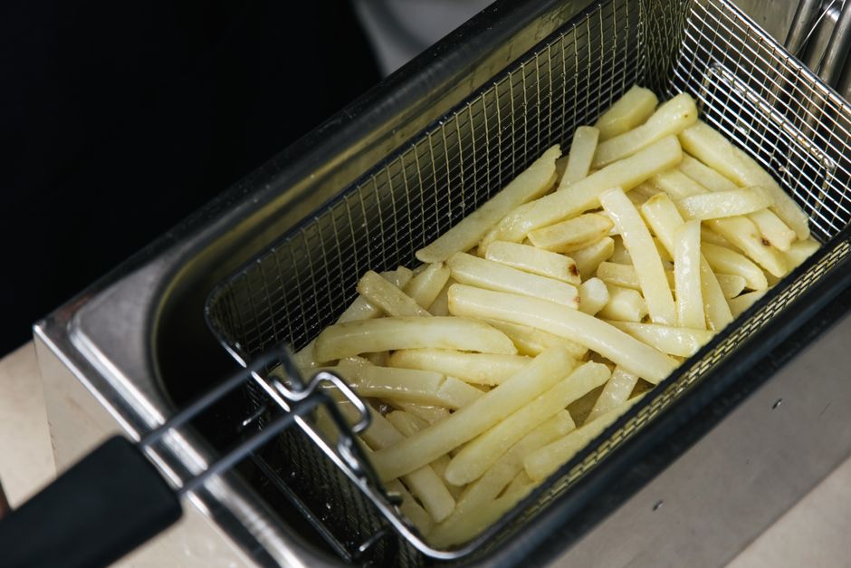 Close-up of raw french fries in a deep fryer basket ready for cooking.