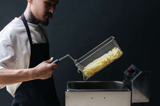 A chef uses a deep fryer to cook french fries. Indoor cooking scene.