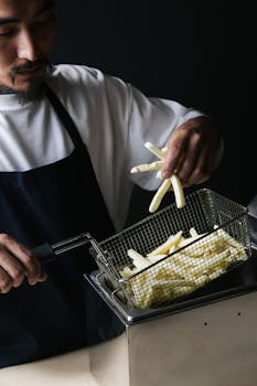 Asian chef placing raw potatoes in deep fryer to make French fries.