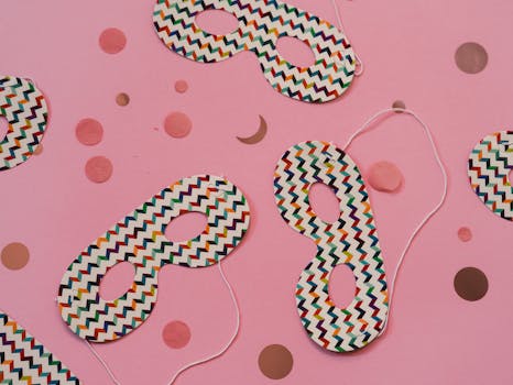 Festive carnival masks with zigzag patterns on a pink surface with polka dots.