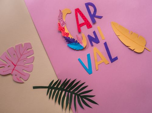 Free Vibrant paper cutouts and leaves spell out 'Carnival' on a pink surface, creating a festive mood. Stock Photo