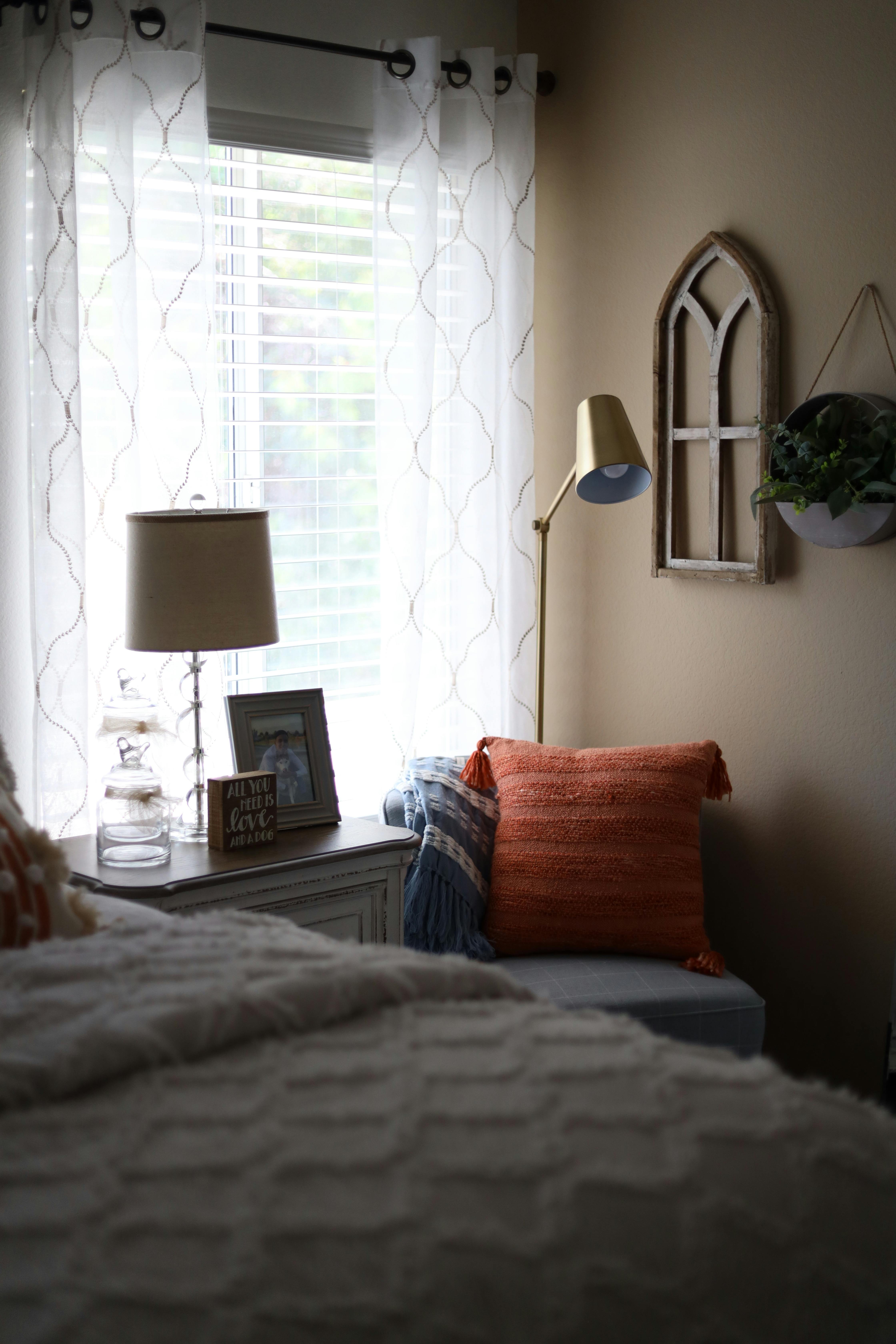 A stylish bedroom corner with a cozy pillow, lamp, and decor items by a bright window.