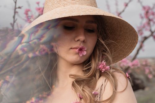 Free Close-up of a woman in a straw hat surrounded by pink blossoms. Stock Photo