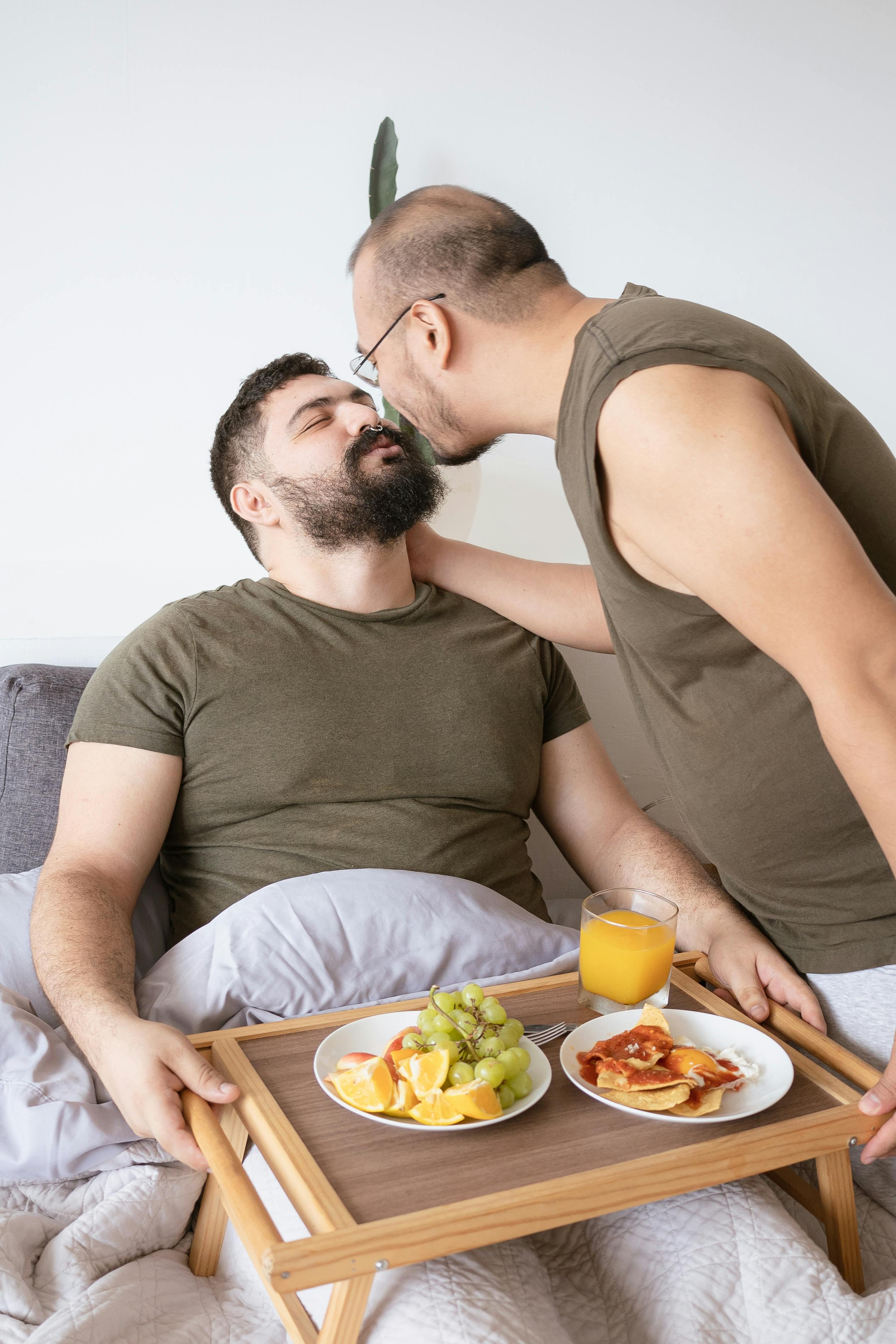 man in brown shirt sitting on bed while holding brown wooden tray