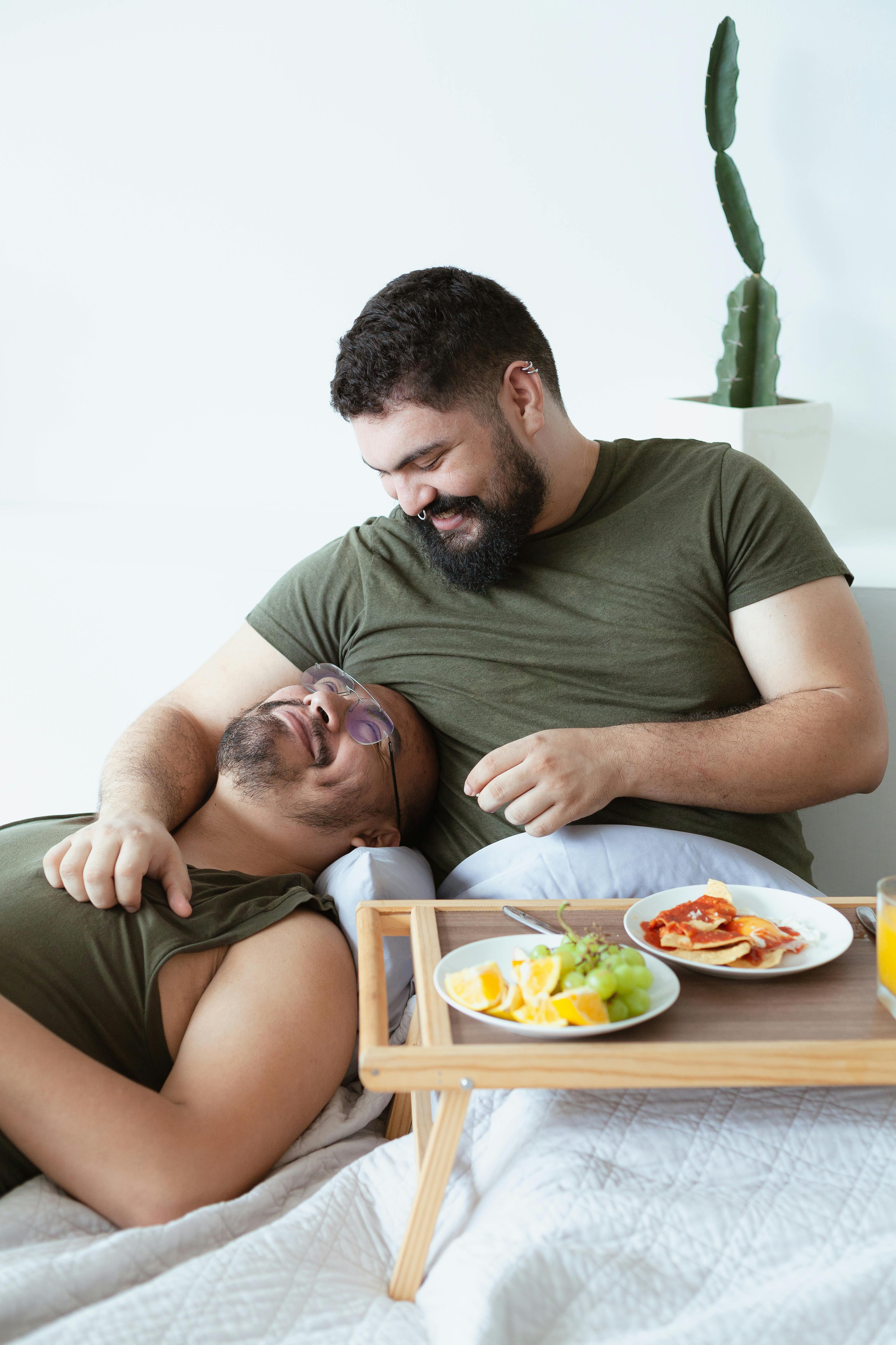 A loving couple shares a joyful moment over breakfast in bed with fresh fruit and pancakes.