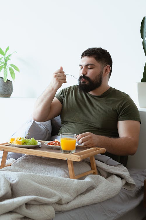 Free Man in Green Shirt Eating on Bed Stock Photo