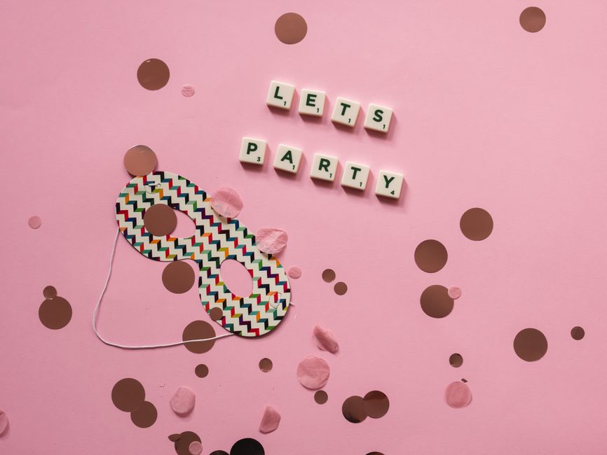 A colorful party mask with confetti and Scrabble tiles spelling