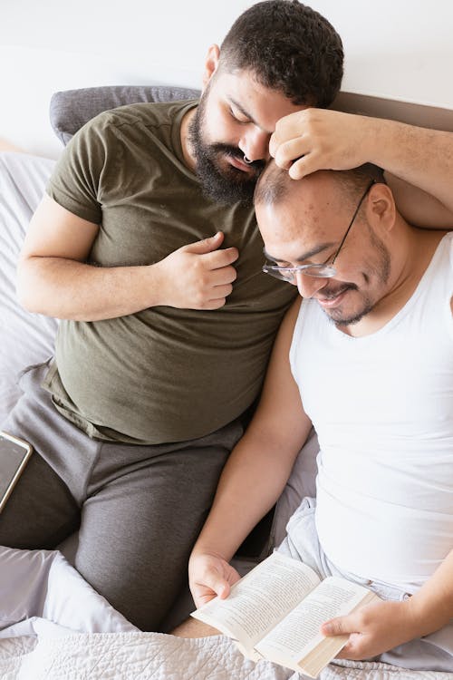 Free Man Showing Affection to Another Man Reading a Book Beside Him Stock Photo