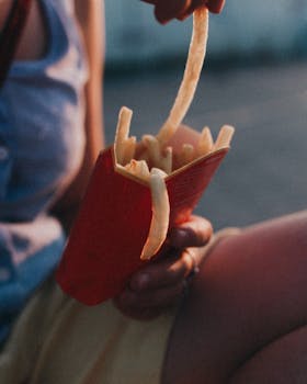 Young adult holding french fries outdoors, capturing a casual summer snack moment.