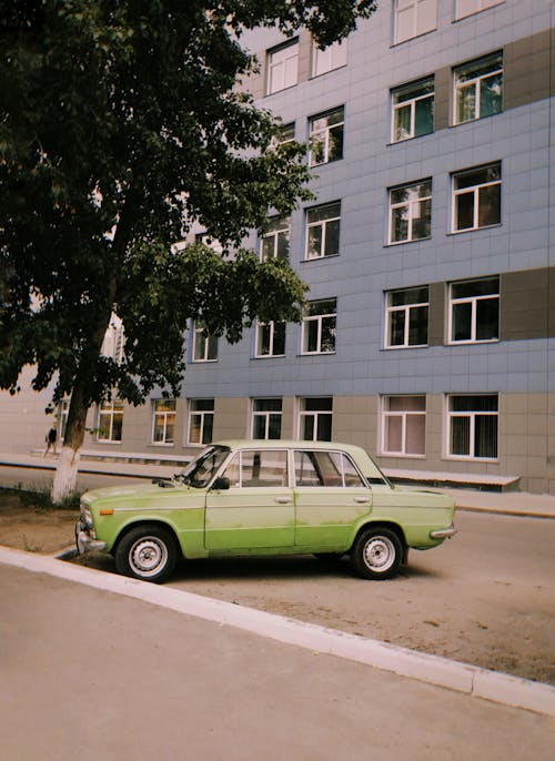 Old Car Parked Beside Green Tree in front of a Building