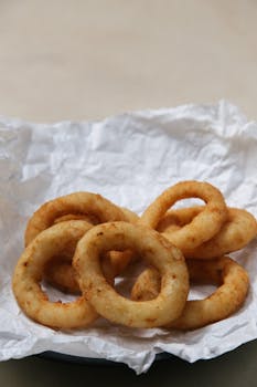 Close-up of crispy golden fried onion rings served on crumpled parchment paper.