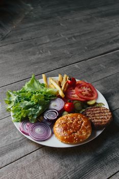 Plate with burger ingredients and fries on textured wooden table. Perfect for culinary and food photography.