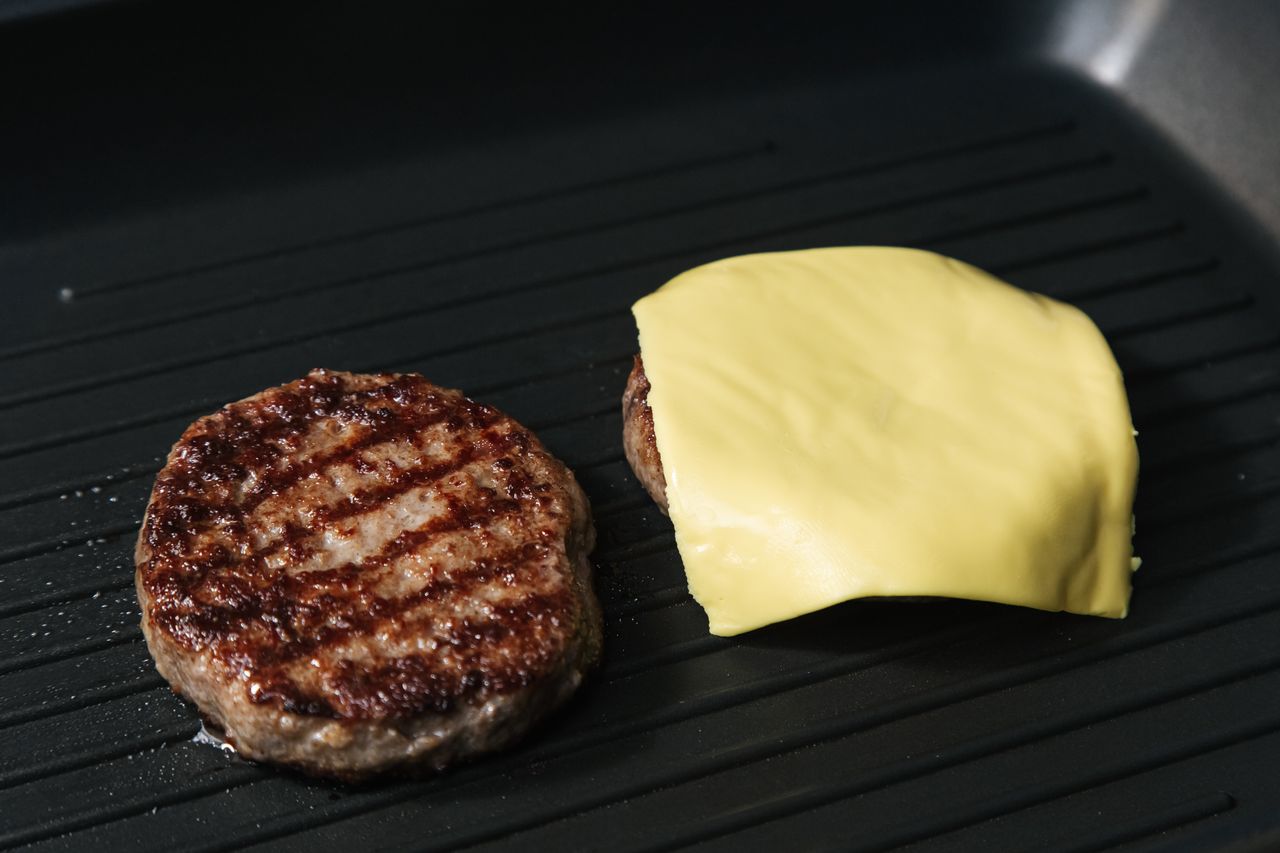 close up of grilled burger patties on a pan one topped with melted che