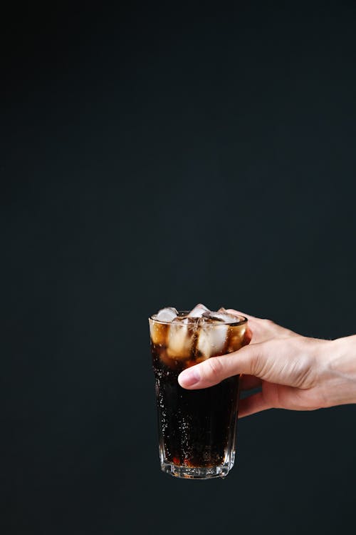 Photo of a Person's Hand Holding a Glass with Cola