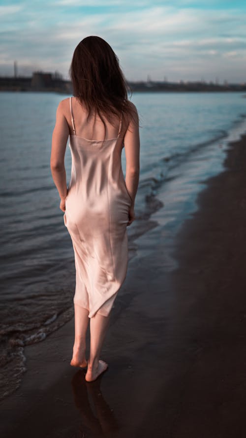 Free Back View of a Woman in a Silk Dress Walking at the Beach Stock Photo