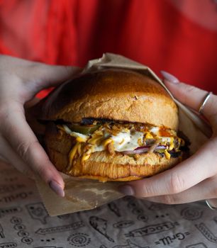 Tasty hamburger held by hands with a red shirt in background, perfect for food photography.