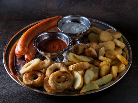 Delicious platter of sausages, fries, and dips served on a stainless steel plate.
