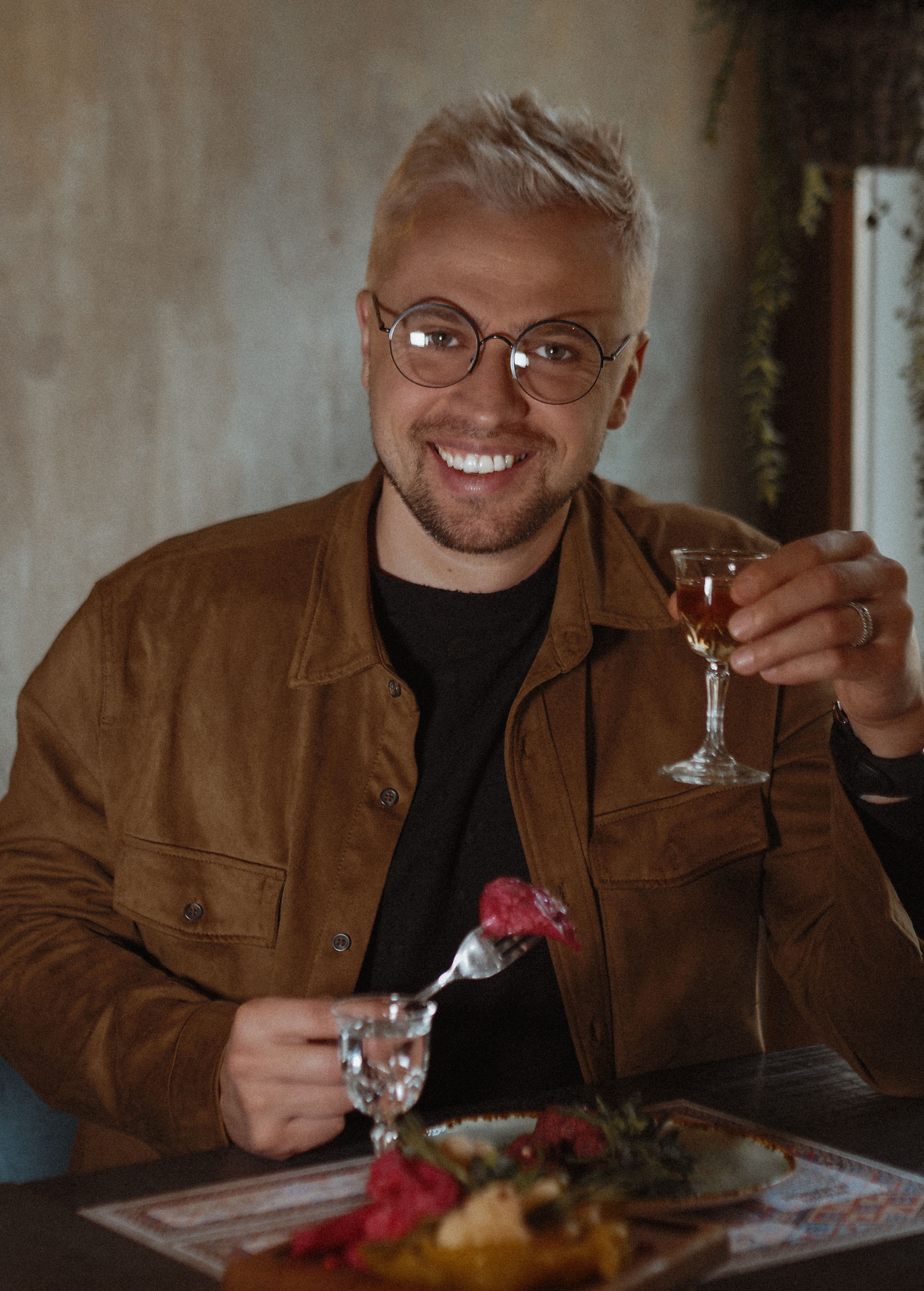 A cheerful man enjoys a meal and wine indoors, capturing a warm moment.