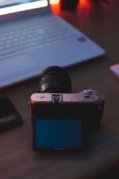 Free A camera and laptop on a wooden desk during evening light, creating a creative workspace atmosphere. Stock Photo
