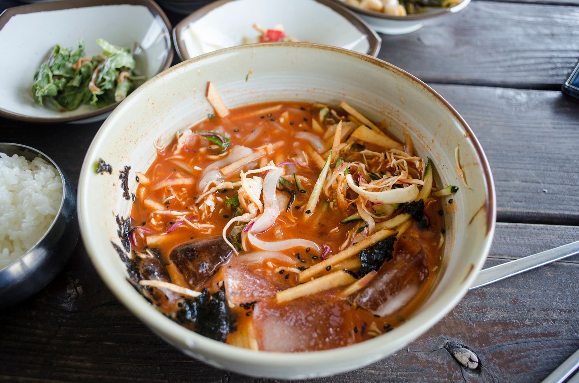 A close-up shot of a bowl of Korean Chogye-guksu, with chilled broth, white noodles, and shredded chicken.