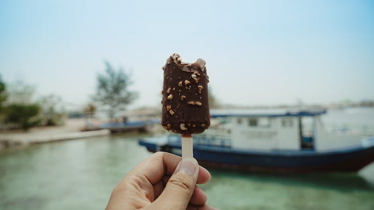 Person Holding Chocolate Ice Cream Bar With A Bite