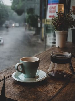 Coffee cup and pot on a wooden table by the window on a rainy day, creating a cozy ambiance.
