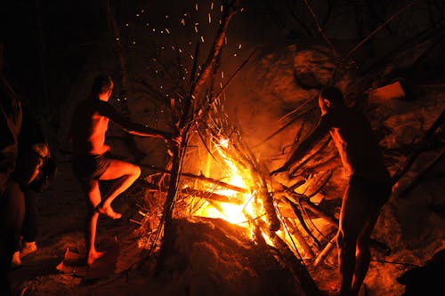 Two Shirtless Men Standing Near a Campfire 