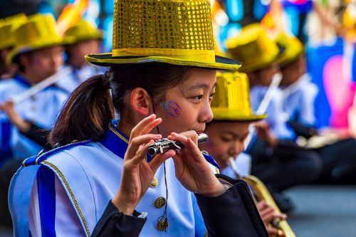 Free A focused young musician playing the flute in a colorful outdoor parade setting. Stock Photo