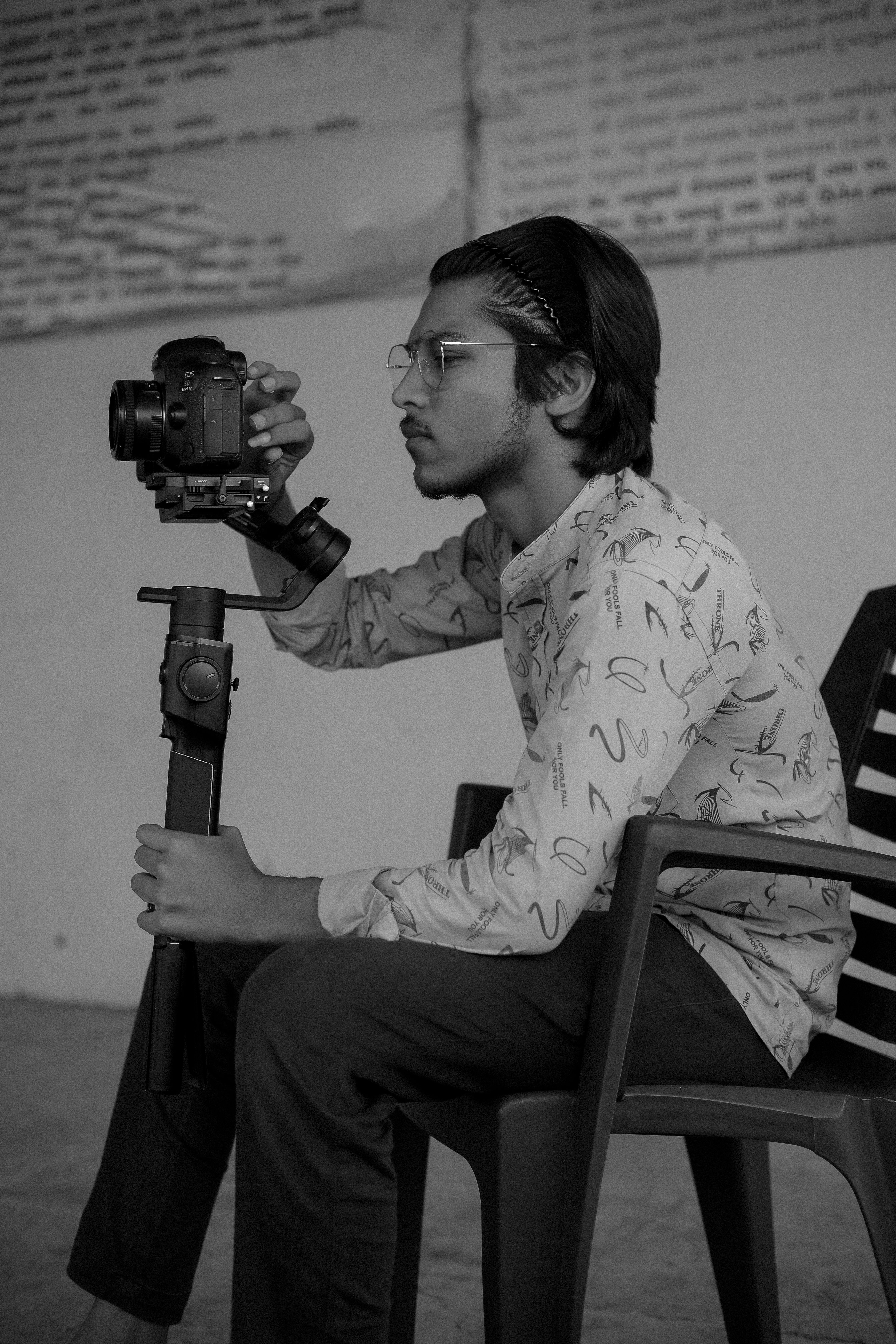 Young photographer sitting and adjusting camera on gimbal in a monochrome setting.
