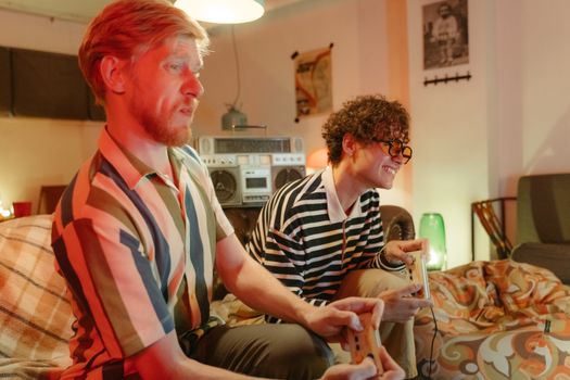 Two men playing video games on a sofa, enjoying leisure time indoors.