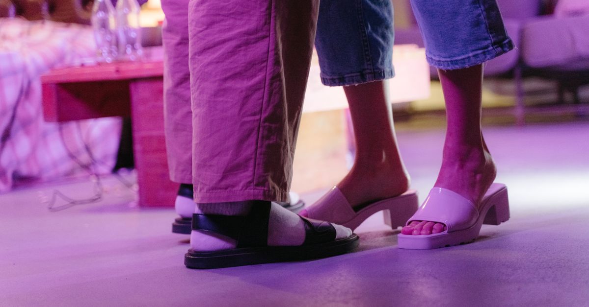 Casual close-up of a couple's feet indoors with purple lighting and stylish footwear.