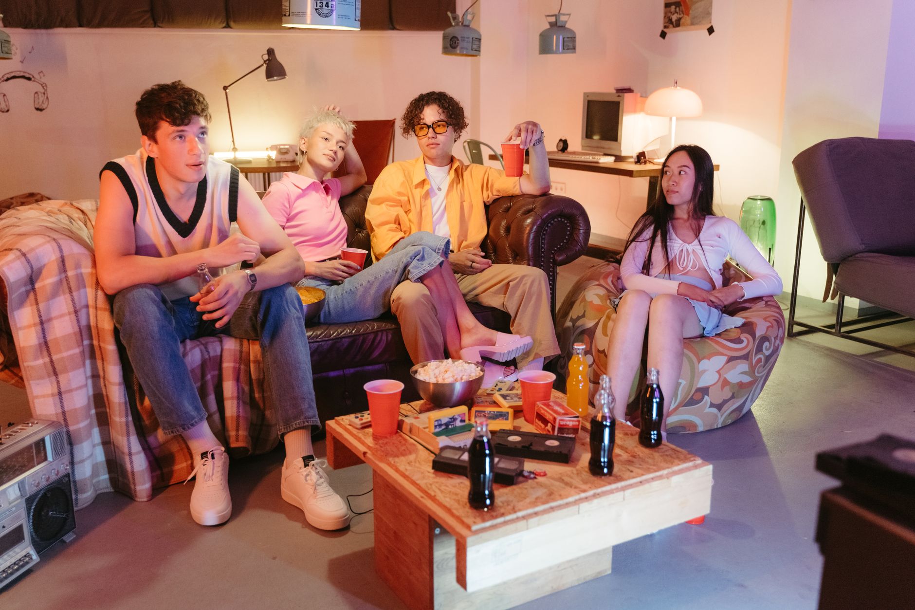 Group of teenagers enjoying a retro-themed hangout with snacks and drinks indoors.