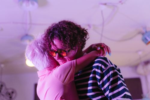 Free A diverse couple shares a joyful hug indoors with vibrant lighting and unique fashion. Stock Photo