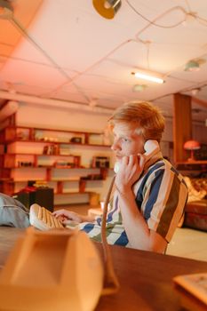 A young man using a retro landline phone in a warm, cozy office setting with bookshelves.