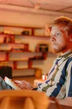 Bearded man reading in a modern, cozy setting with warm lighting. Ideal for lifestyle content.
