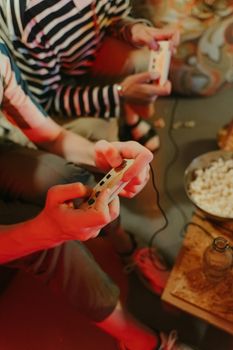 Two friends playing video games with classic controllers, surrounded by snacks, having fun indoors.