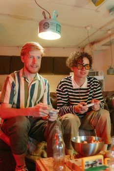 Two men relax while playing video games indoors, surrounded by a cozy atmosphere.