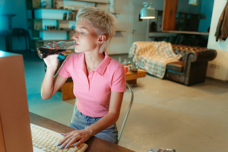 A Woman Drinking A Bottle Of Soda While Typing On A Computer Keyboard