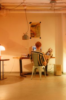 A man sits at a vintage desk using a retro computer in a warmly lit room.