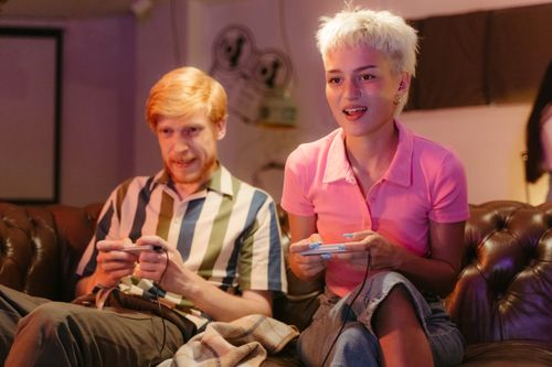 Free Two friends enthusiastically playing video games on a vintage sofa indoors. Stock Photo
