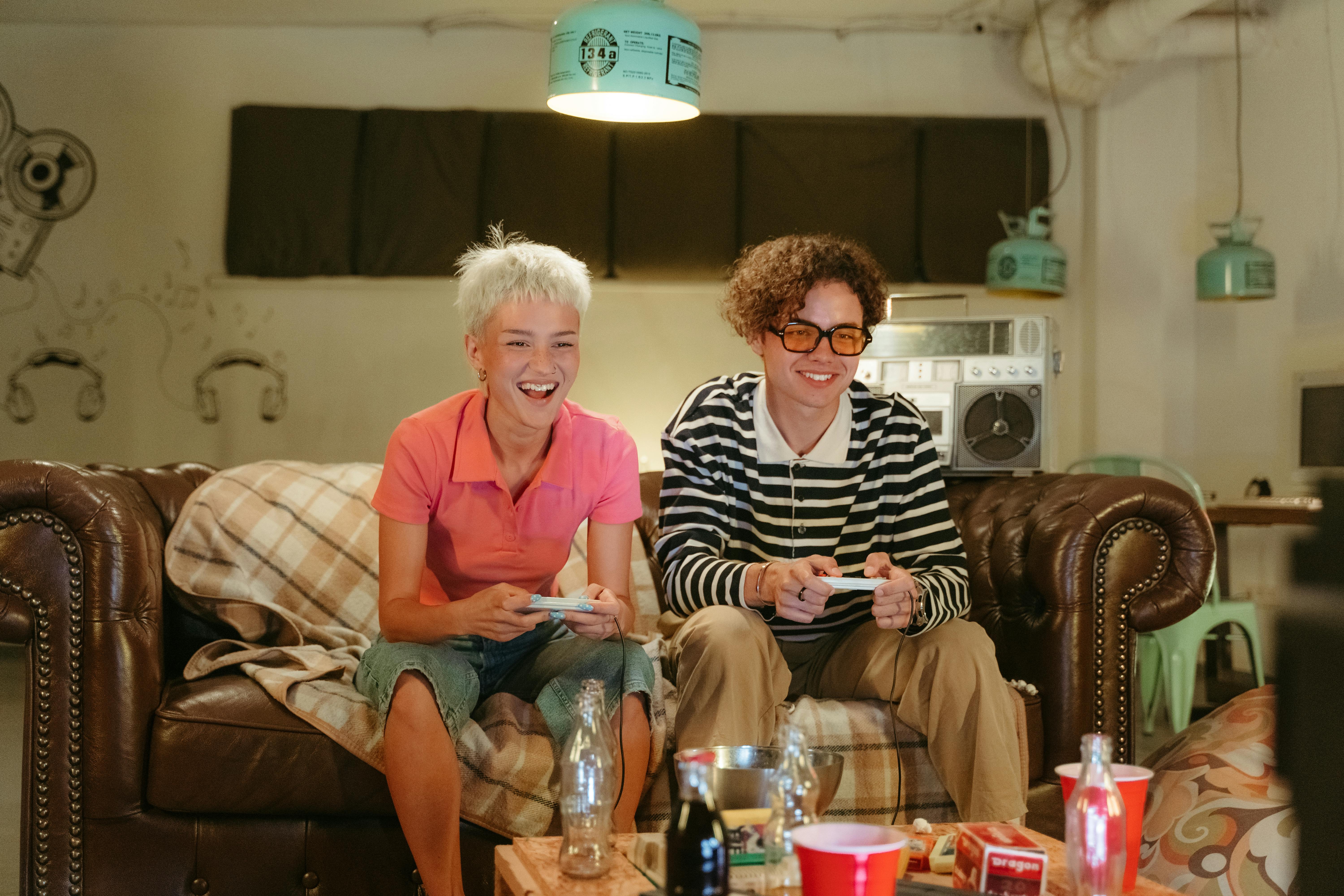 teenage boy and girl sitting on brown couch playing video game console