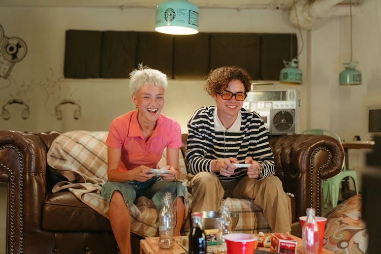 Teenage Boy And Girl Sitting On Brown Couch Playing Video Game Console